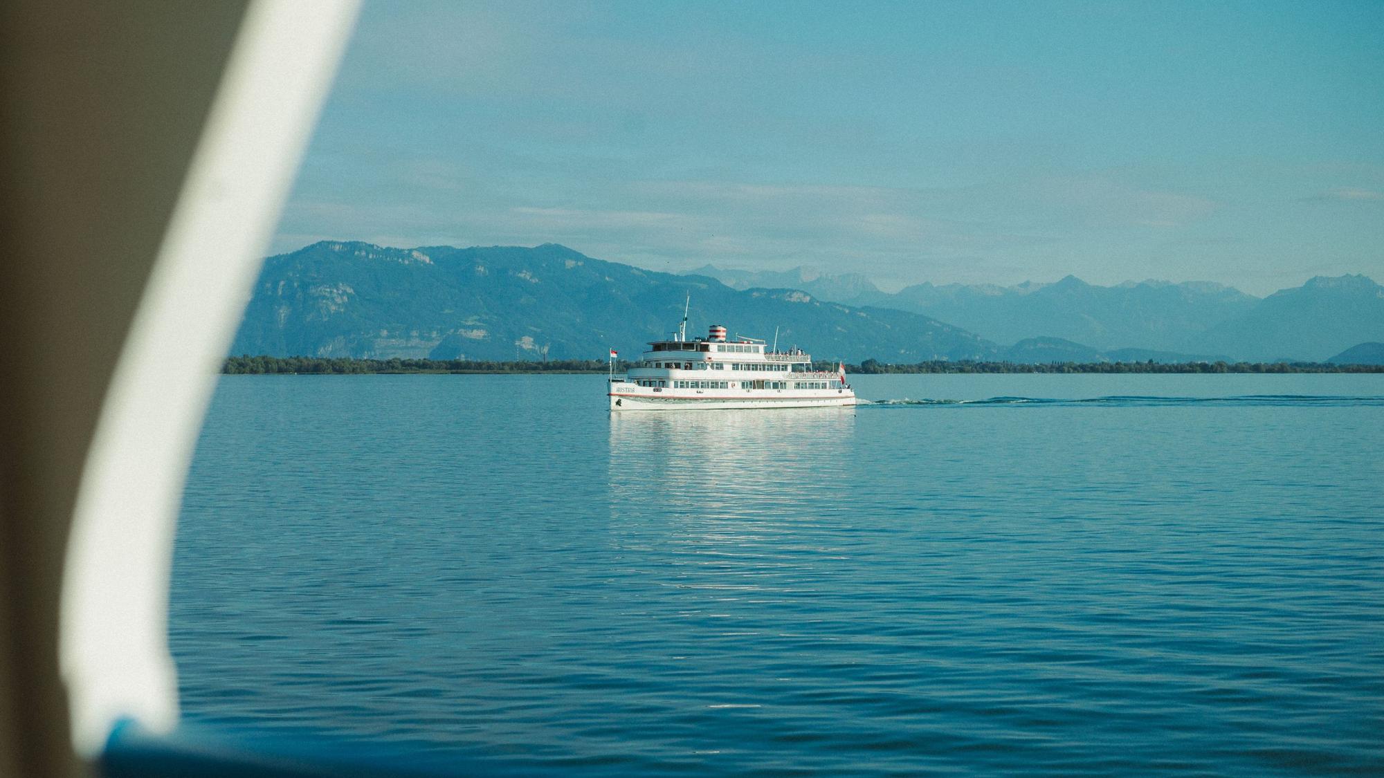 Ein weißer Ausflugsdampfer fährt über einen tiefblauen See vor einer Gebirgssilhouette vorbei.