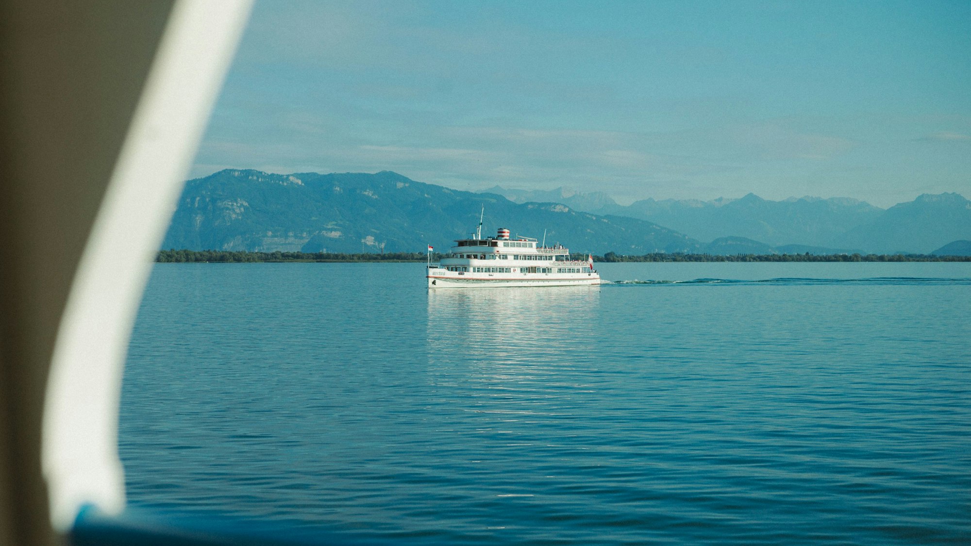 Ein weißer Ausflugsdampfer fährt über einen tiefblauen See vor einer Gebirgssilhouette vorbei.