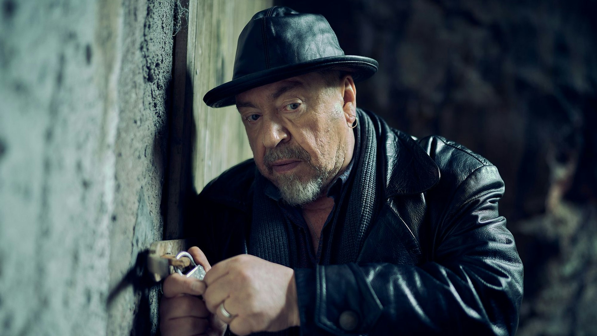 Ein Mann in Lederjacke mit einem Lederhut auf dem Kopf öffnet ein Vorhängeschloss.