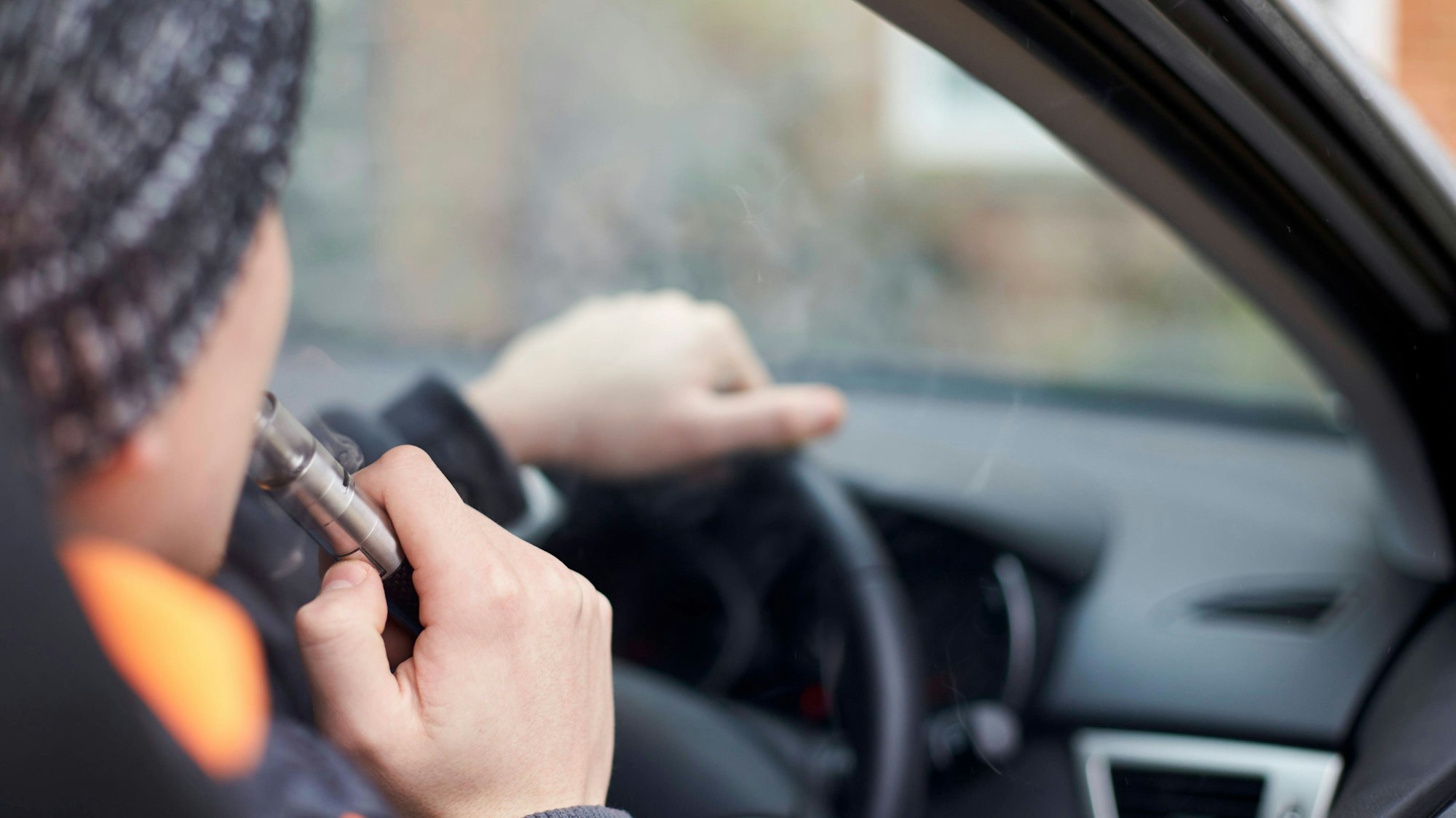 Ein Autofahrer raucht während der Fahrt eine E-Zigarette.