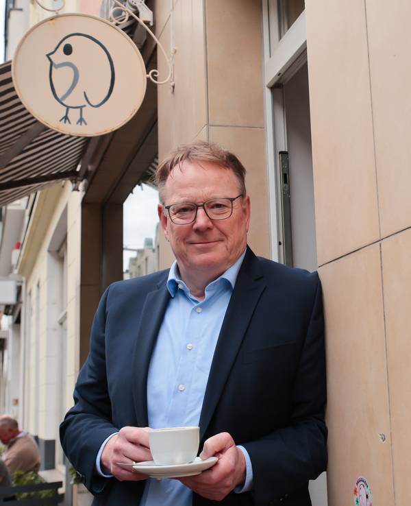 Torsten Burmester lehnt mit einer Kaffeetasse an einer Hauswand.