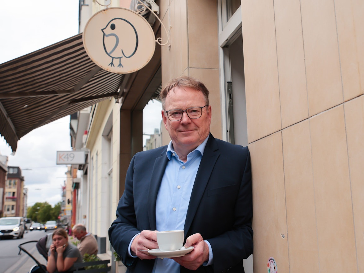 Torsten Burmester lehnt mit einer Kaffeetasse an einer Hauswand.