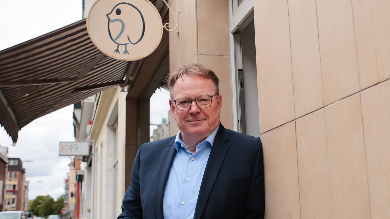 Torsten Burmester lehnt mit einer Kaffeetasse an einer Hauswand.
