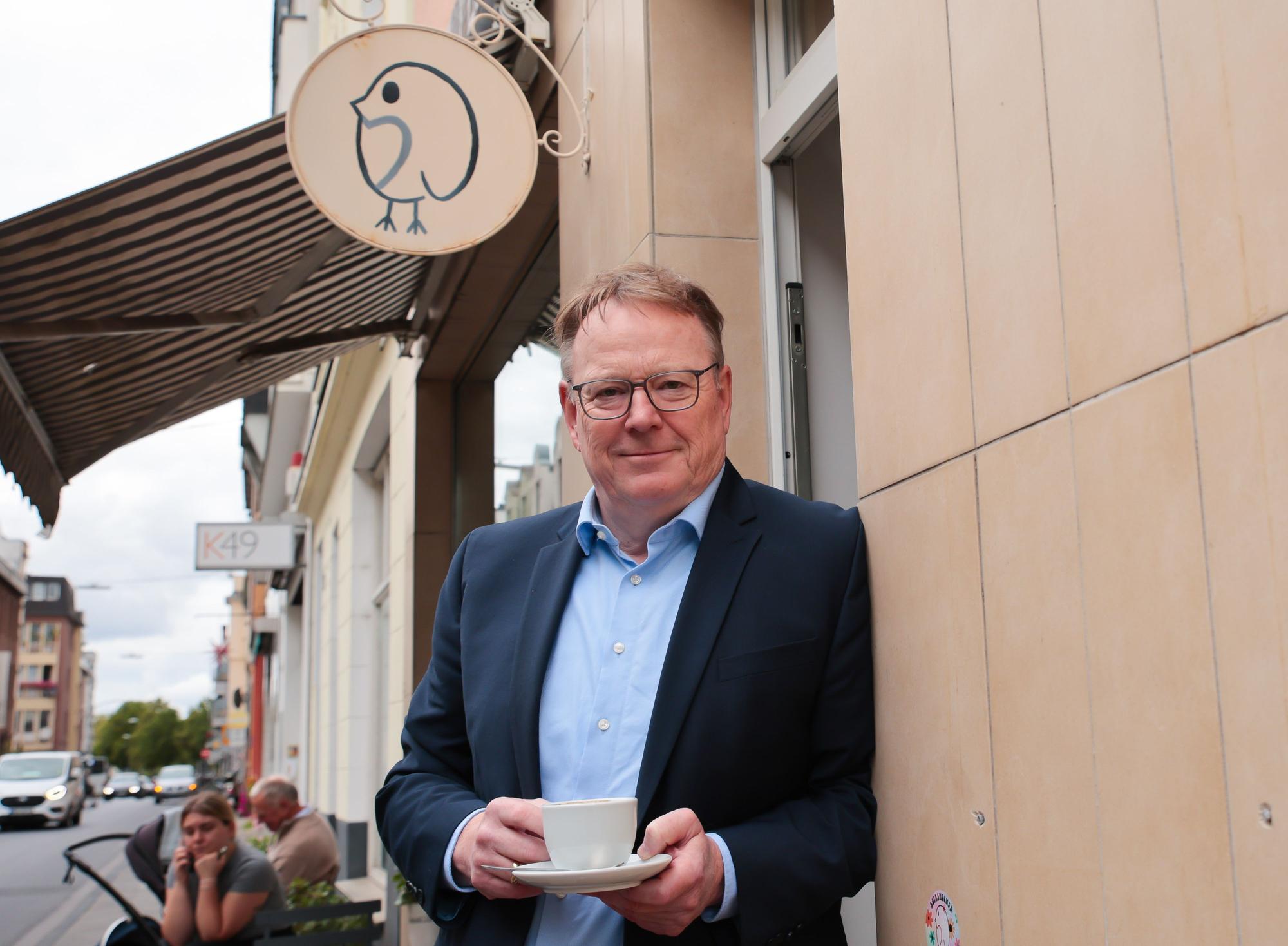 Torsten Burmester lehnt mit einer Kaffeetasse an einer Hauswand.