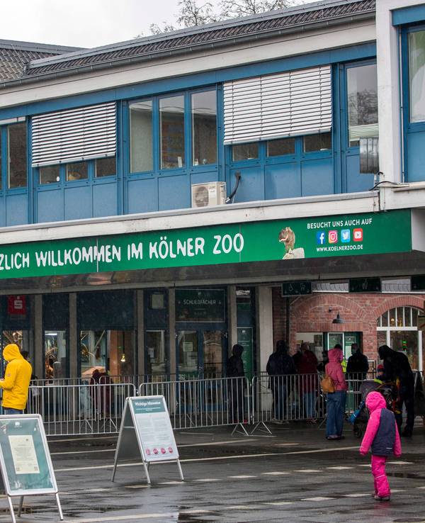Menschen in Regensachen stehen vor dem Haupteingang des Kölner Zoos.