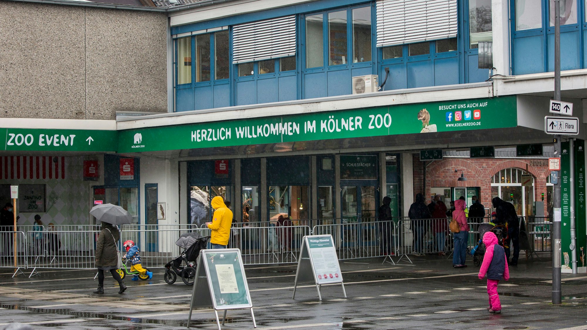 Menschen in Regensachen stehen vor dem Haupteingang des Kölner Zoos.