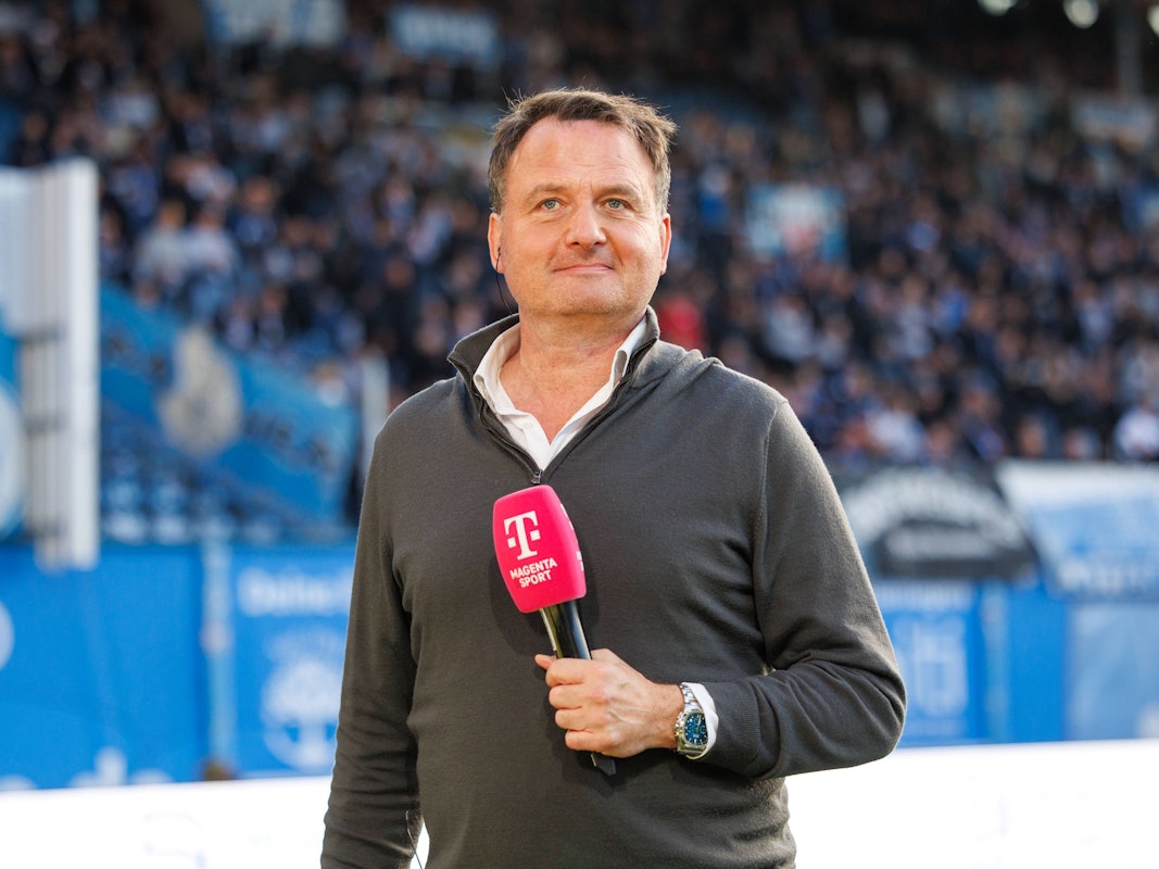 Magenta-Moderator Thomas Wagner steht mit seinem Mikrofon am Spielfeldrand.