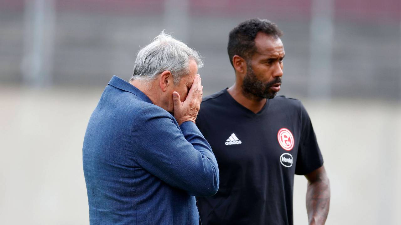Daniel Thioune steht auf dem Trainingsplatz von Fortuna Düsseldorf neben F95-Boss Klaus Allofs, der die Hände vor das Gesicht schlägt.