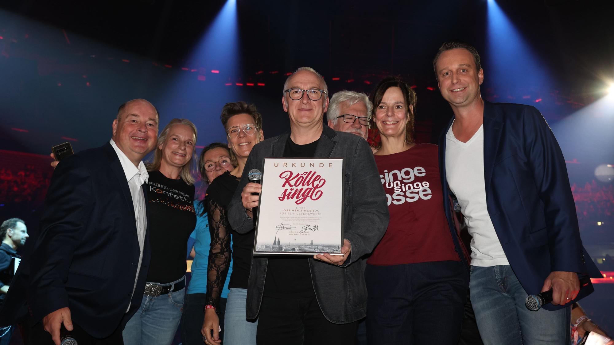 Das Team von „Loss mer singe“ steht mit Urkunde auf der Bühne.