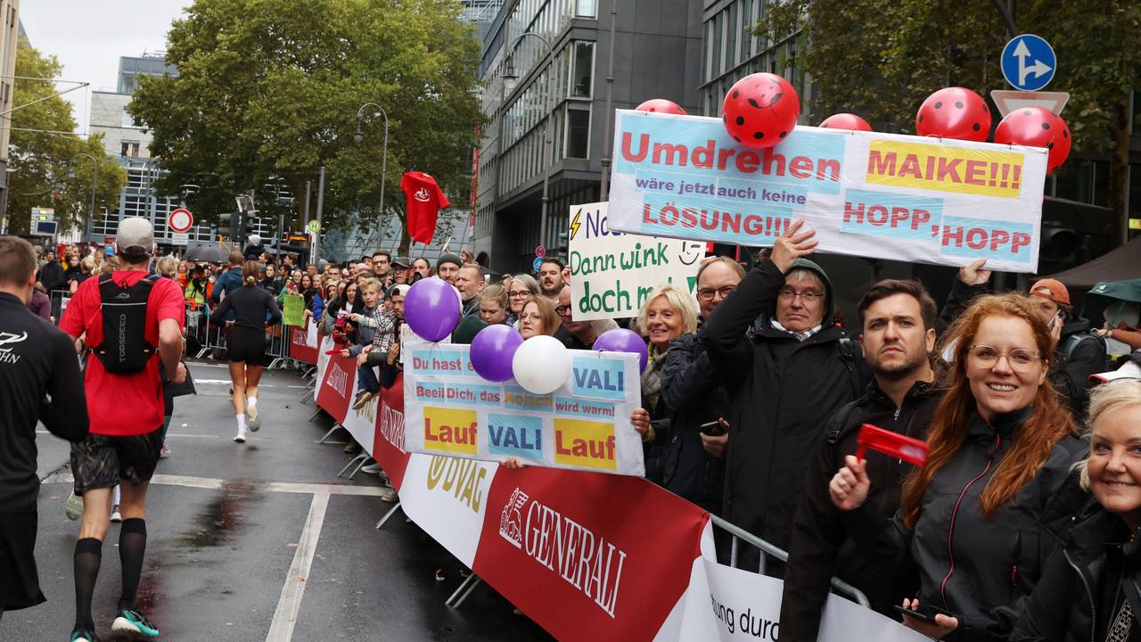 Zuschauer halten am Streckenrand des Köln-Marathons Schilder hoch, auf denen sie Maike und Vali anfeuern. „Umdrehen wäre jetzt auch keine Lösung“ steht auf einem Schild.