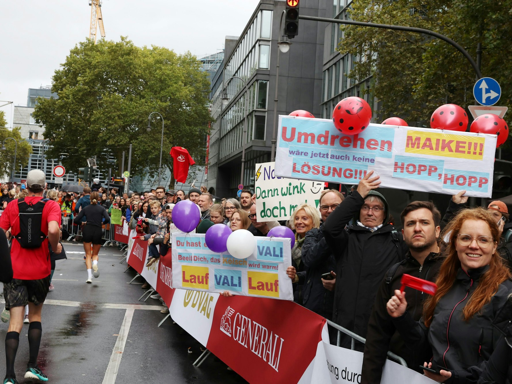 Zuschauer halten am Streckenrand des Köln-Marathons Schilder hoch, auf denen sie Maike und Vali anfeuern. „Umdrehen wäre jetzt auch keine Lösung“ steht auf einem Schild.