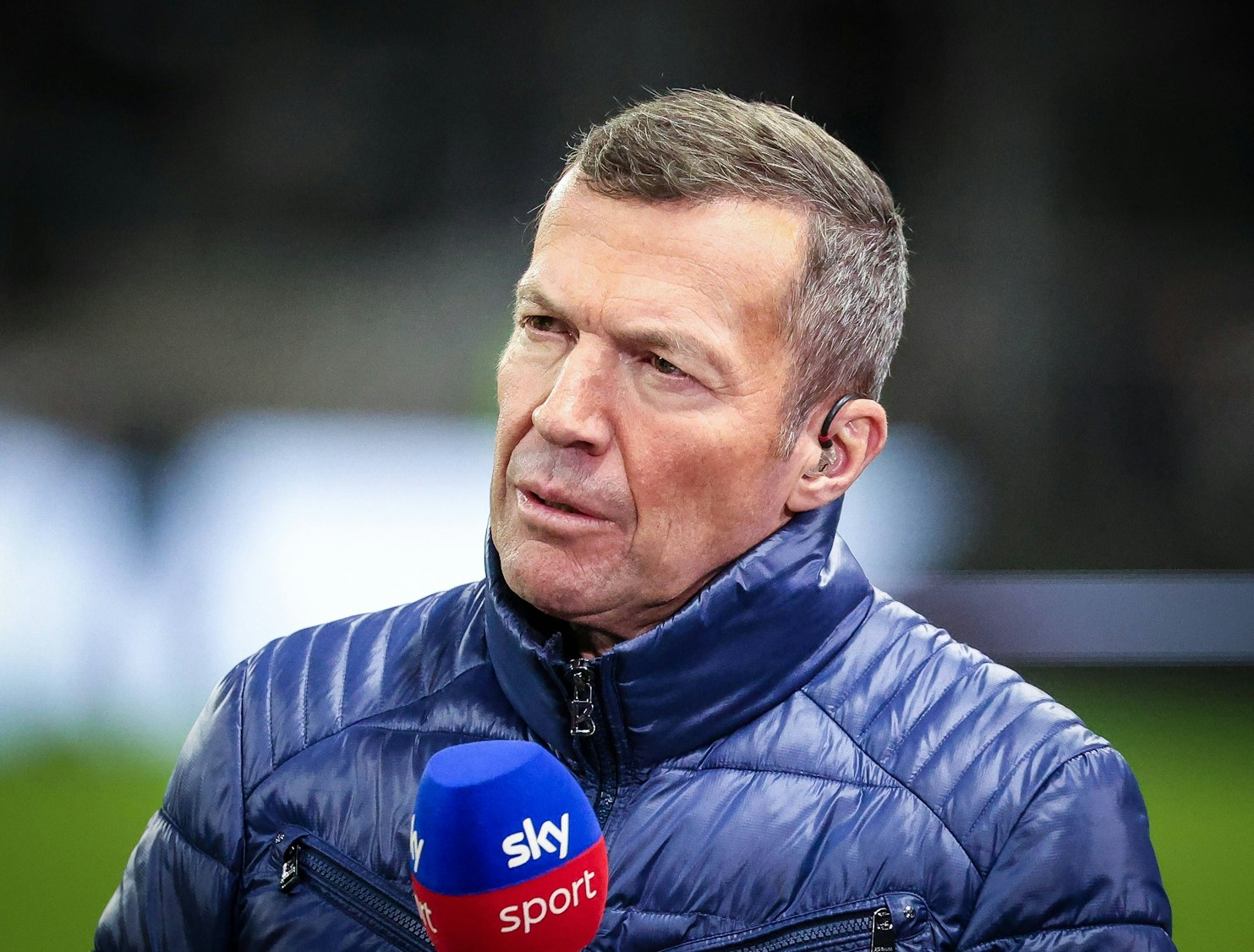 Lothar Matthäus in einer blauen Jacke mit Sky Sport Mikrofon und In-Ear-Kopfhörer