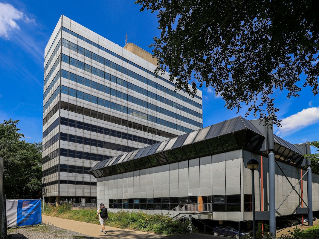 Vor einem Hochhaus steht ein flaches Gebäude.