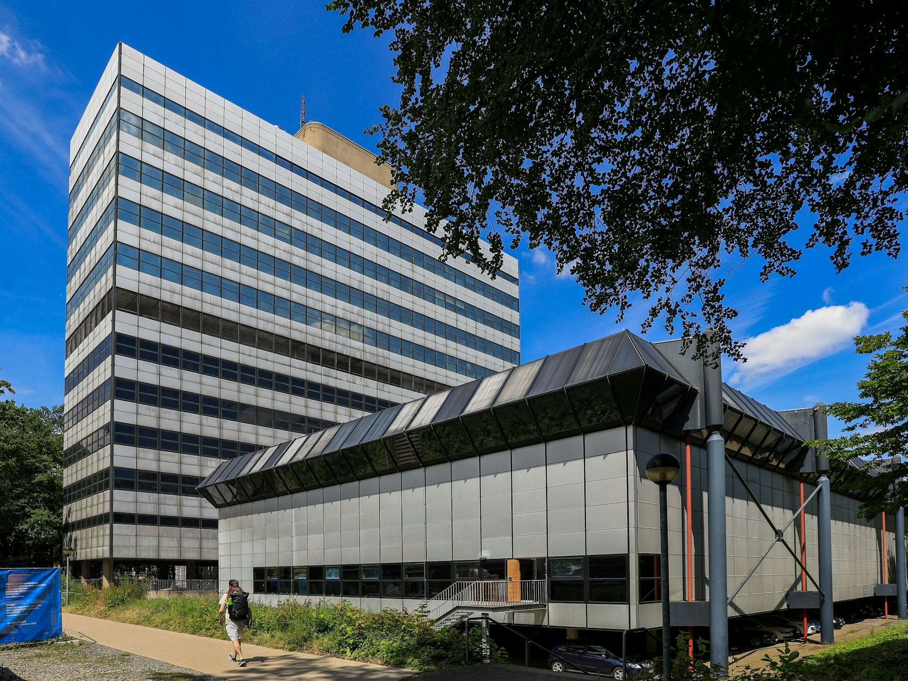 Vor einem Hochhaus steht ein flaches Gebäude.