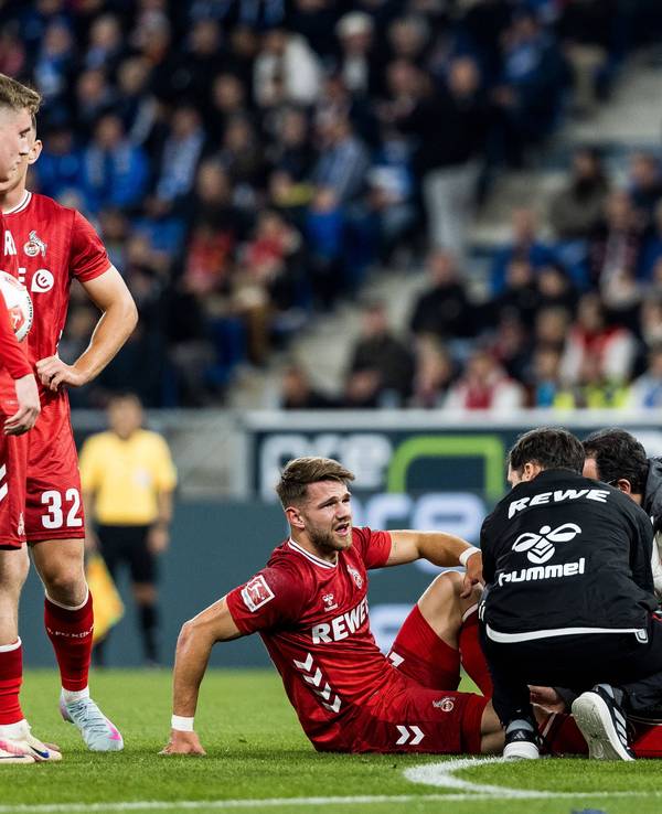 Jan Thielmann wird behandelt, seine FC-Kollegen stehen daneben und schauen zu.