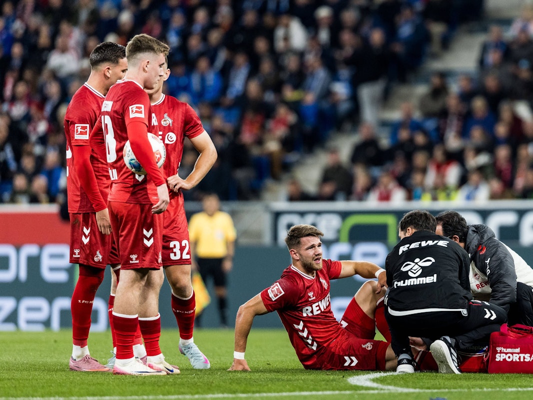 Jan Thielmann wird behandelt, seine FC-Kollegen stehen daneben und schauen zu.