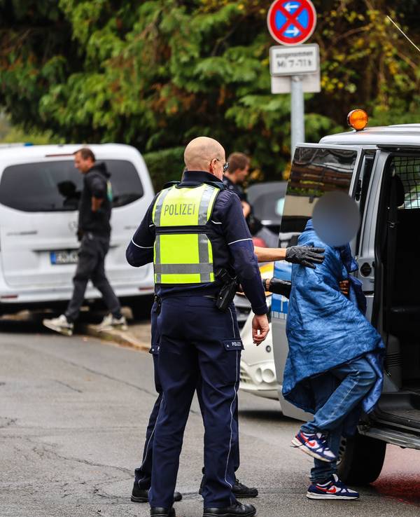 Polizisten bringen einen Jugendlichen zu einem Polizeiauto.