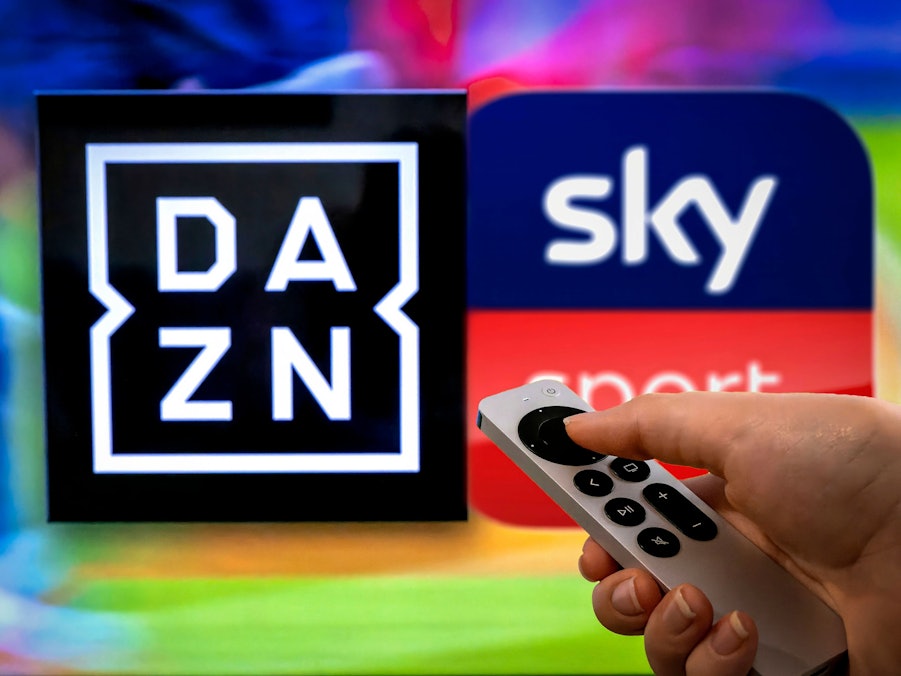 Hand hält Fernbedienung vor Logos von DAZN und Sky Sport