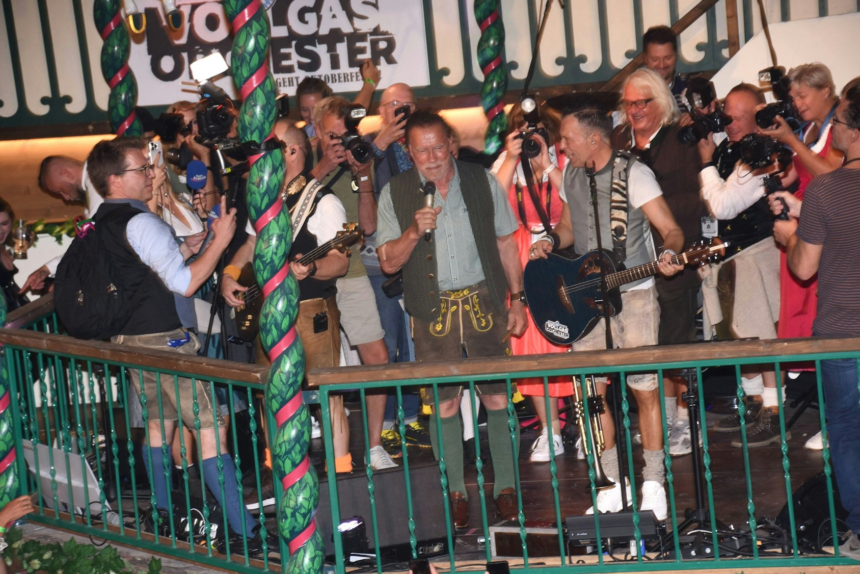 Arnold Schwarzenegger spricht auf der Oktoberfestbühne umgeben von Musikern und Medien