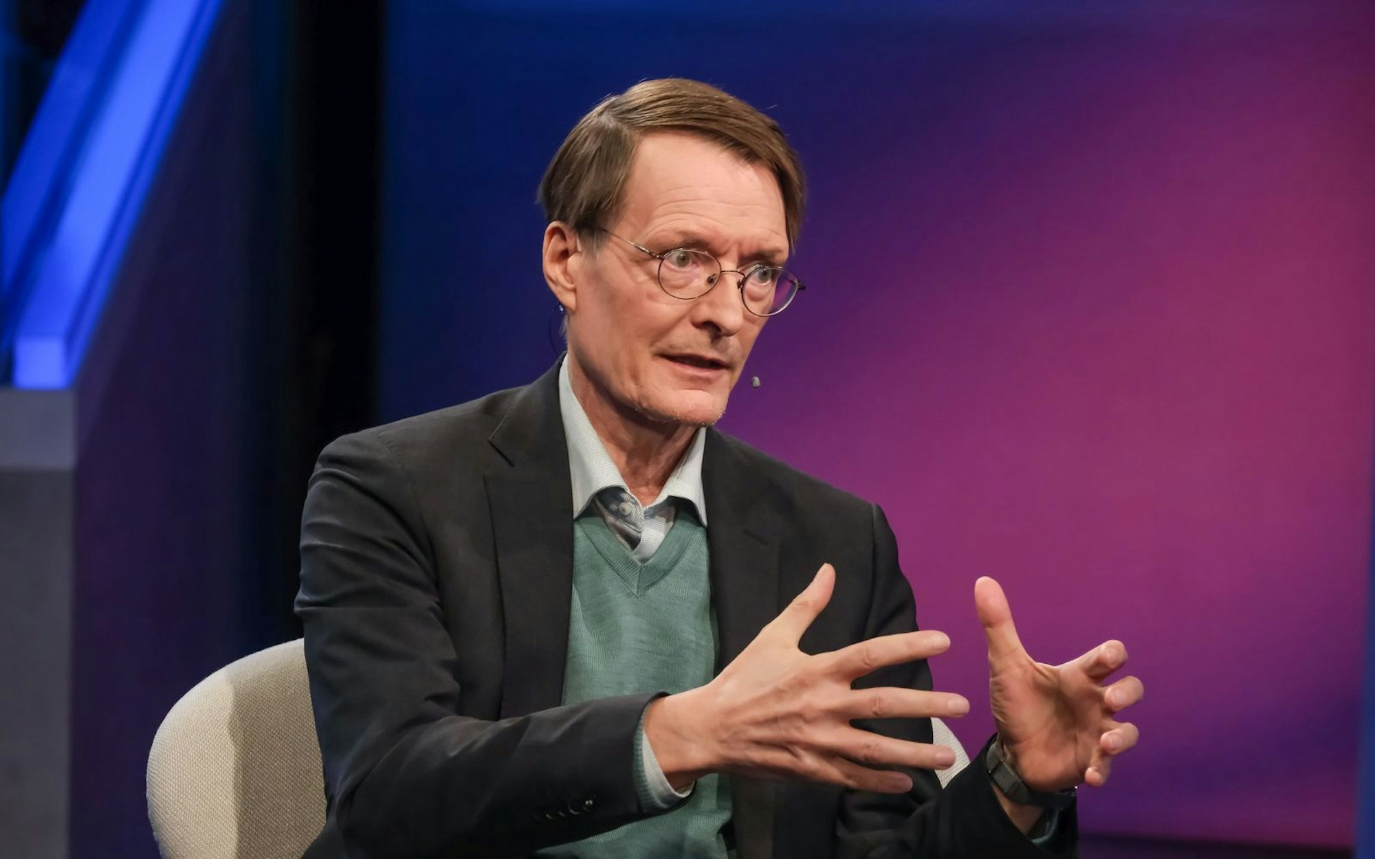 Karl Lauterbach sitzt in einem Fernsehstudio und gestikuliert.