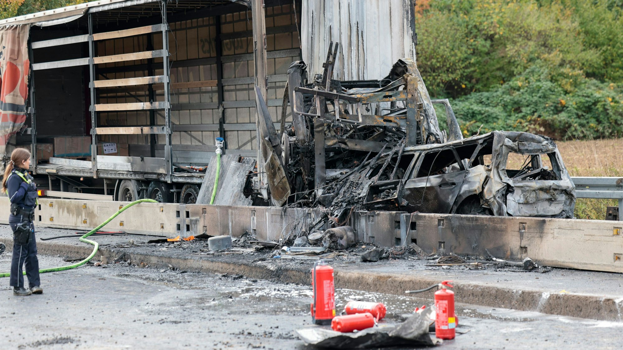 Ausgebrannte Fahrzeugwracks stehen hinter einem halb ausgebrannten Lkw.