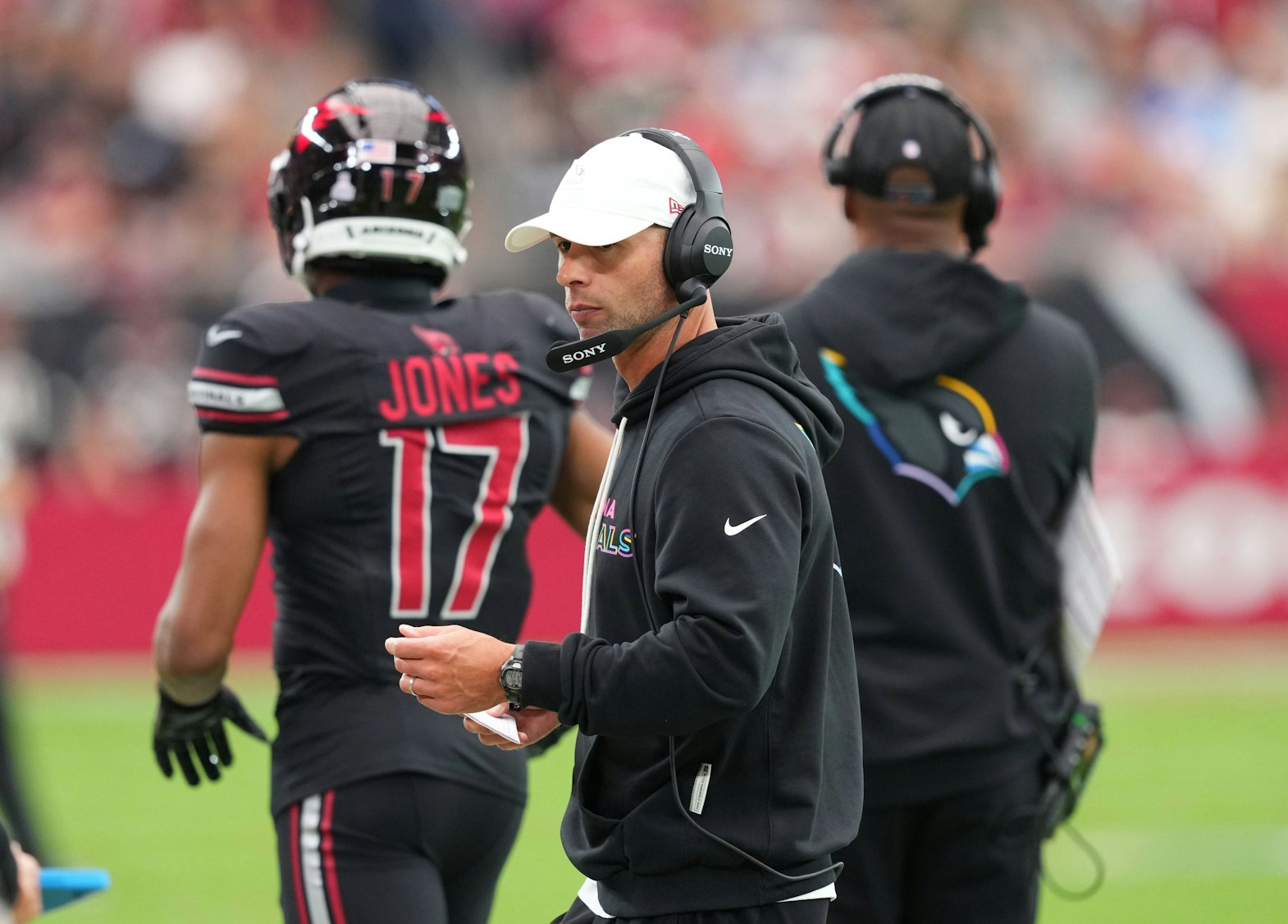 Jonathan Gannon als Trainer mit Headset und Notizen auf dem Footballfeld