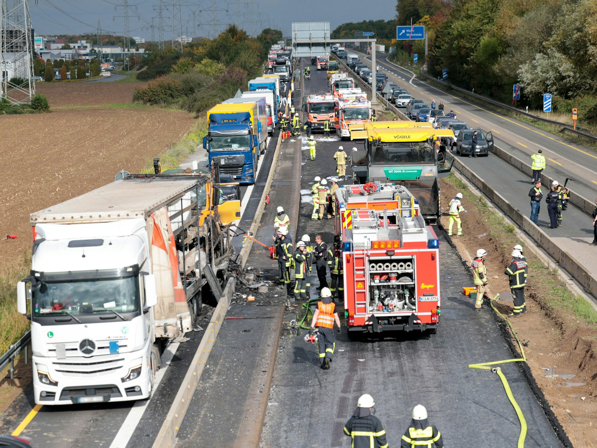 Auf der Autobahn steht ein halb ausgebrannter Lkw, dahinter ein völlig ausgebranntes Fahrzeug. Ein Löschfahrzeug steht daneben, zahlreiche Einsatzkräfte wuseln herum.