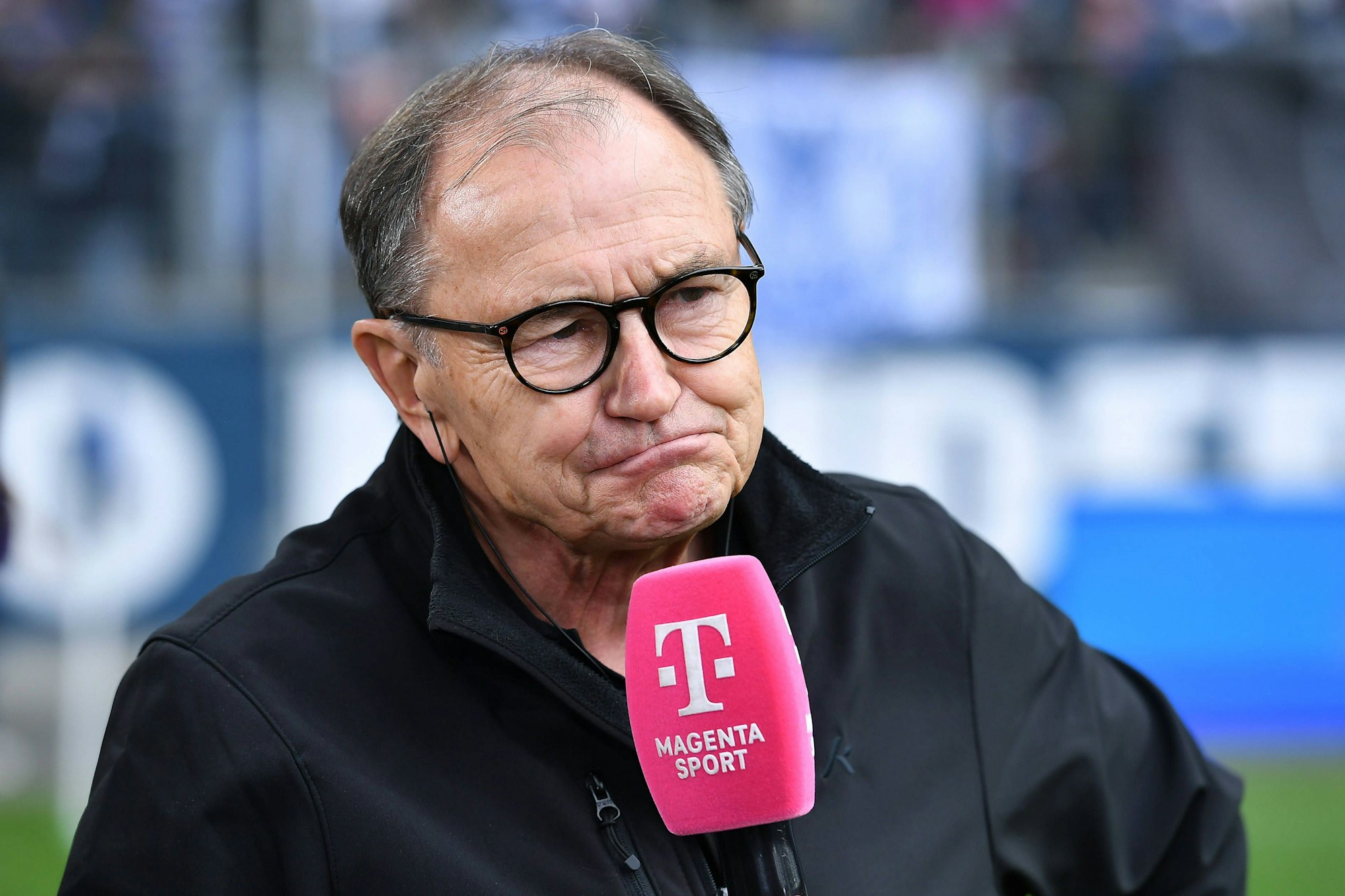 Ewald Lienen sprich in ein Mikro von MagentaSport.