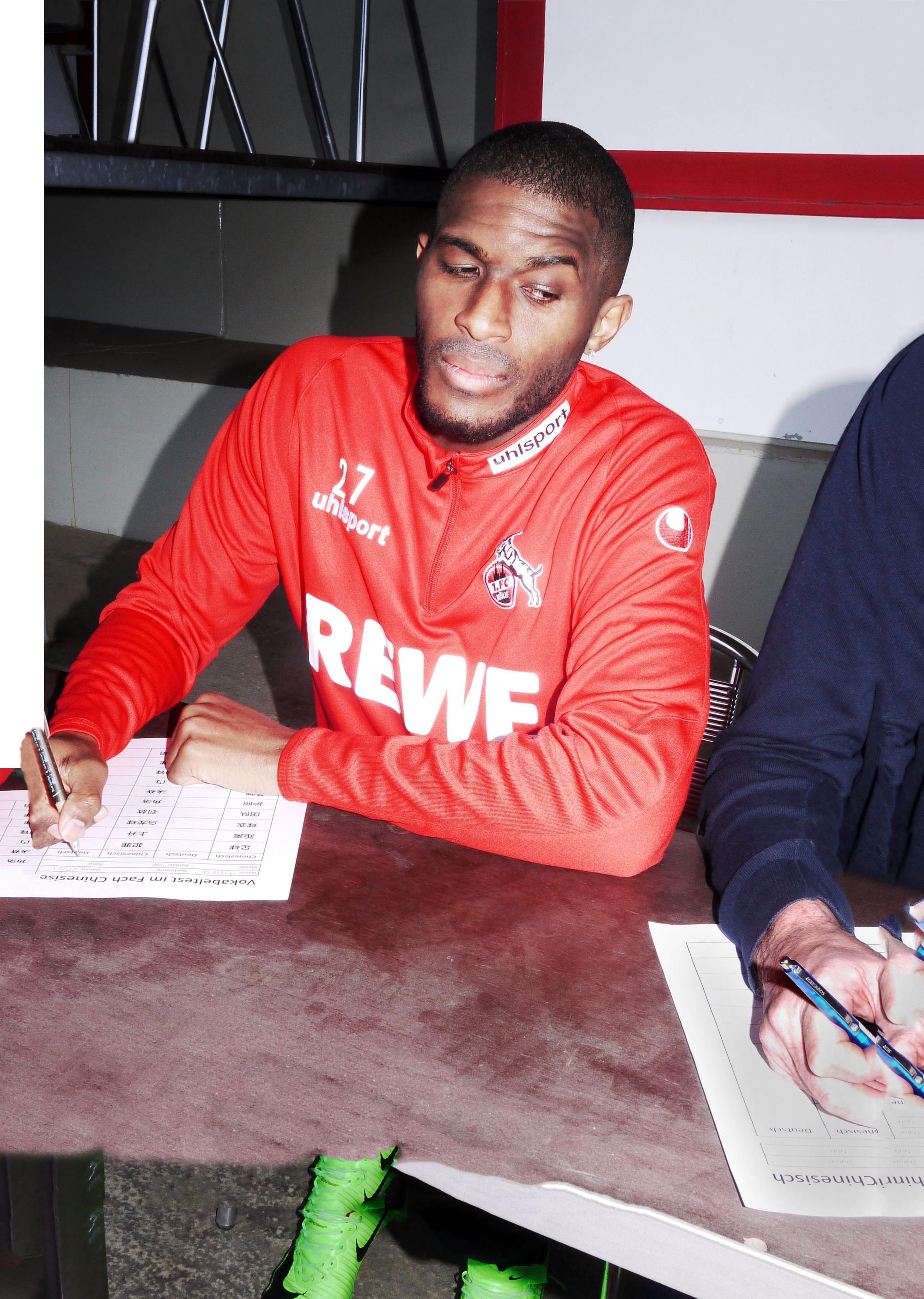 Anthony Modeste posiert für „11FREUNDE LEGENDEN - Die andere Geschichte des 1. FC Köln“ im Trikot mit Zettel und Stift.