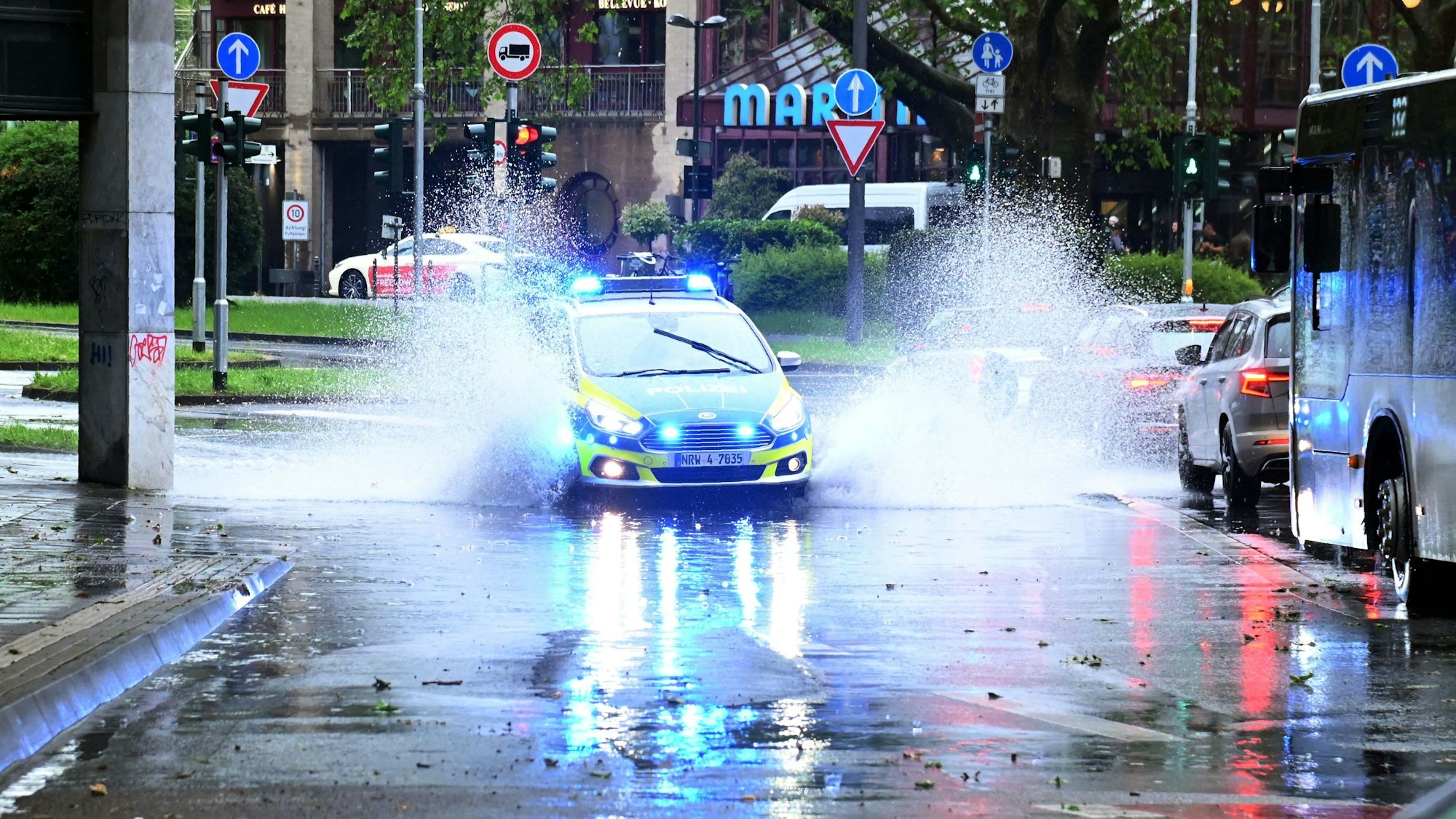 Ein Polizeiauto ist im Einsatz in Köln und fährt durch eine große Regenpfütze.