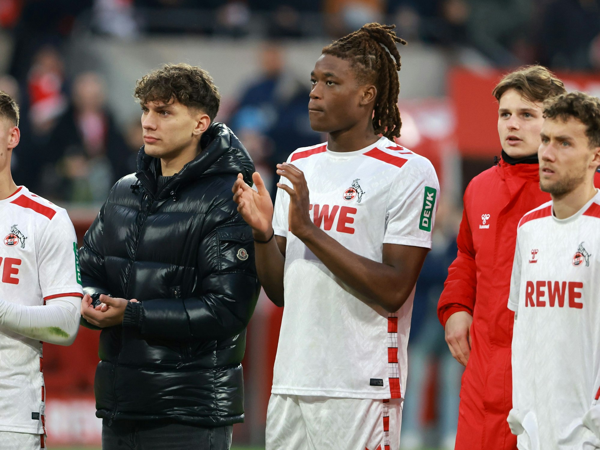 Julian Pauli und Elias Bakatukanda klatschen in die Hände. Pauli trägt eine schwarze Winterjacke, Bakatukanda das Trikot des 1. FC Köln.