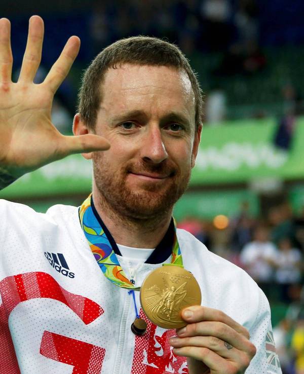 Bradley Wiggins zeigt seine olympische Goldmedaille in die Kamera und zeigt mit seiner rechten Hand die Zahl fünf.