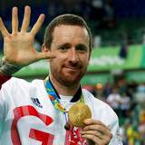 Bradley Wiggins zeigt seine olympische Goldmedaille in die Kamera und zeigt mit seiner rechten Hand die Zahl fünf.