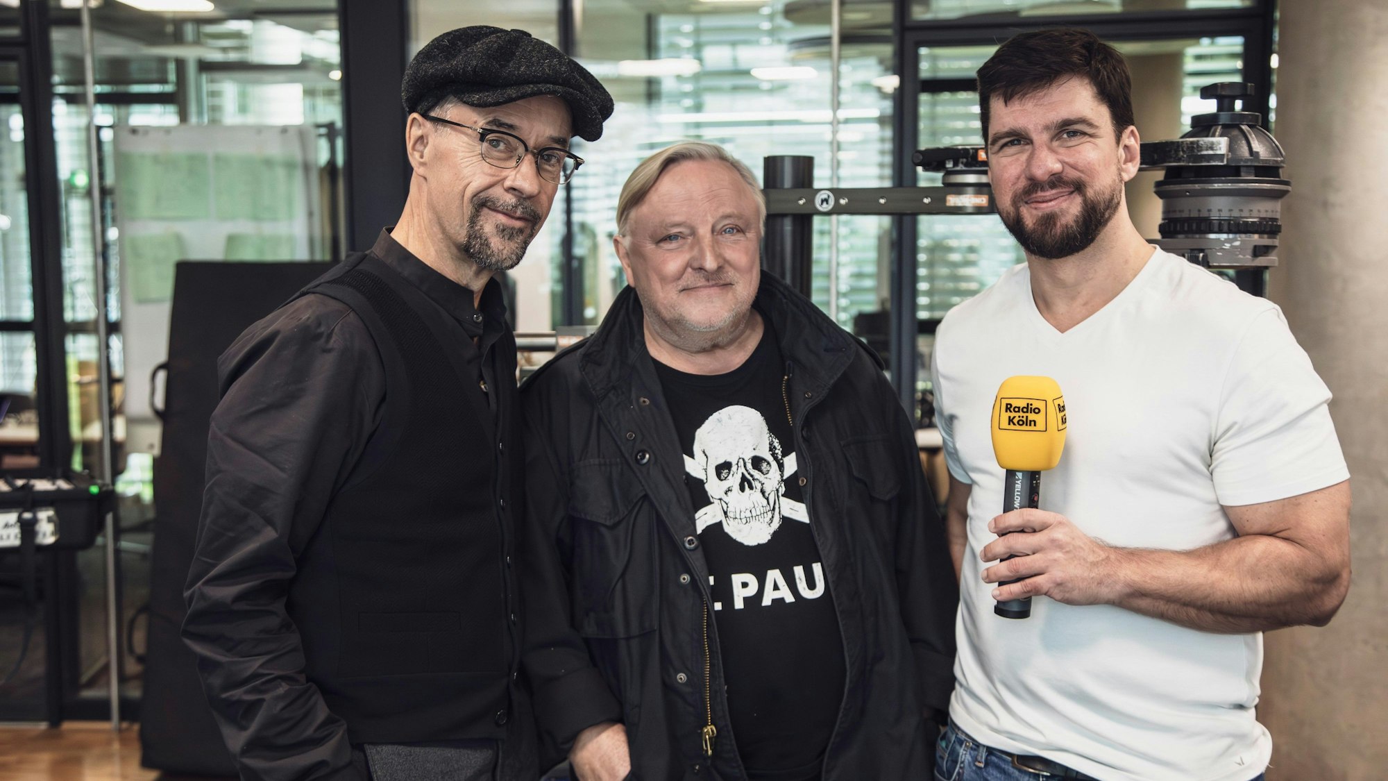 Zwei Schauspieler stehen neben einem Radiomoderator.