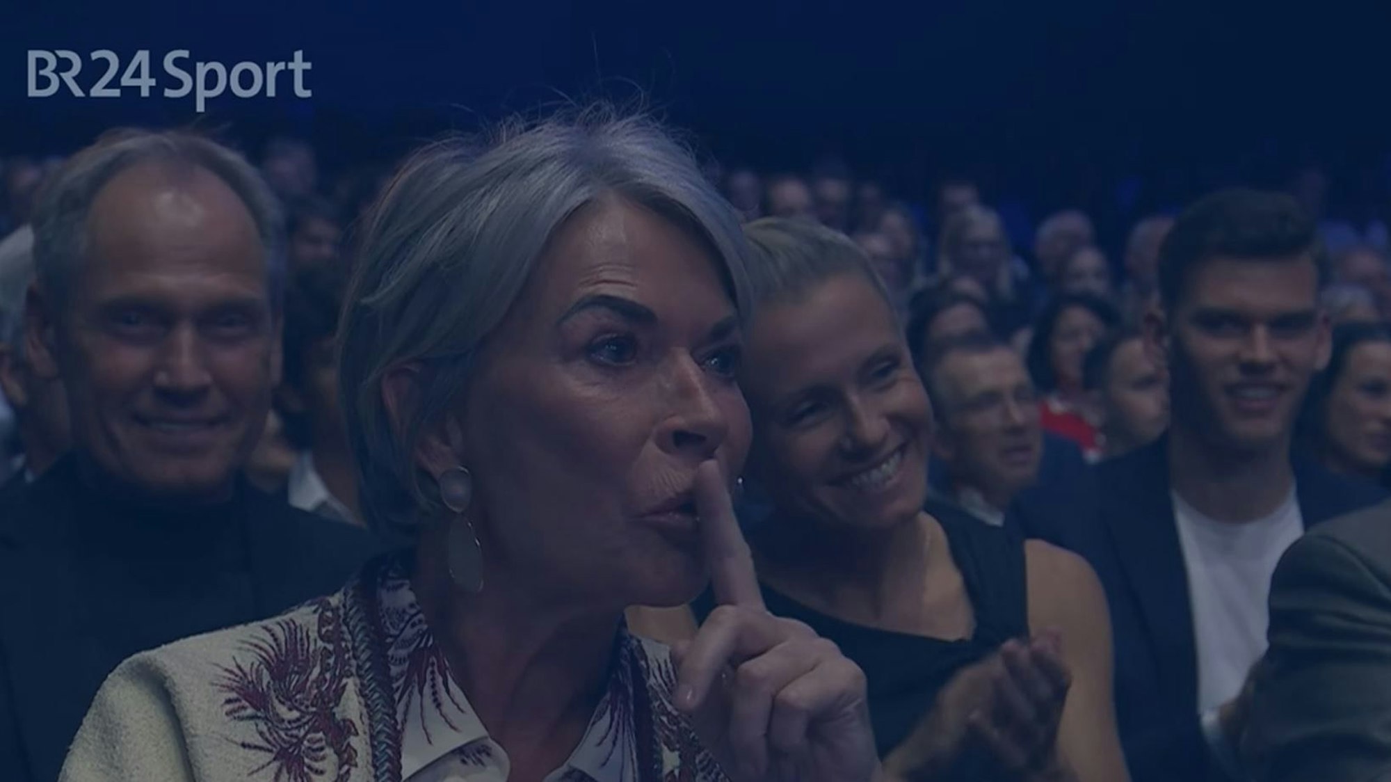Martina Rummenigge legt den Zeigefinger auf ihre Lippen.