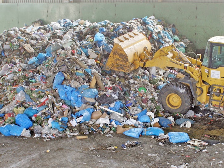 Ein gelber Bagger fährt in den Müll, der sich in einer Hausmülldeponie stapelt.