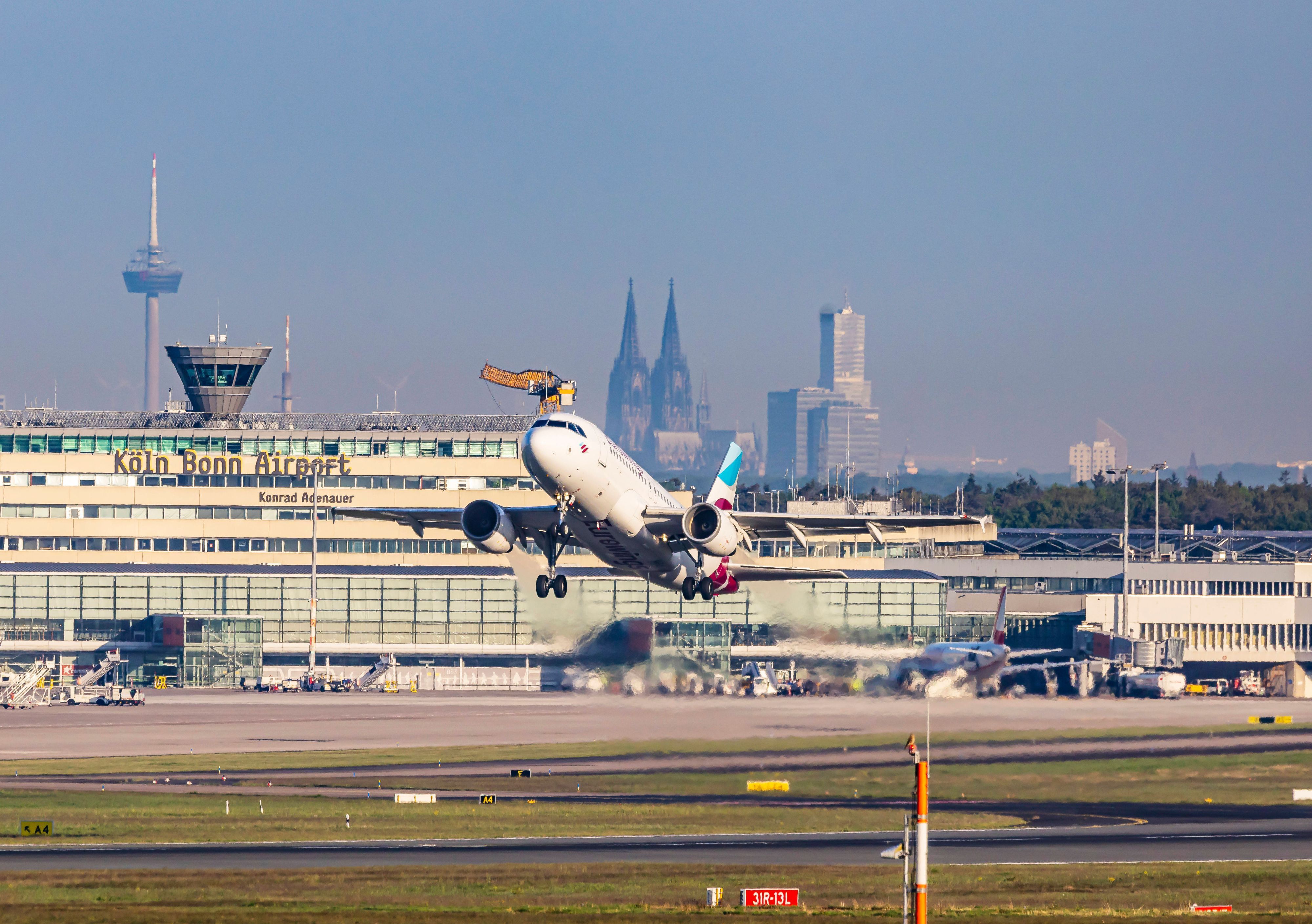 Ein Flugzeug hebt vom Flughafen Köln/Bonn ab. Im Hintergrund der Kölner Dom.