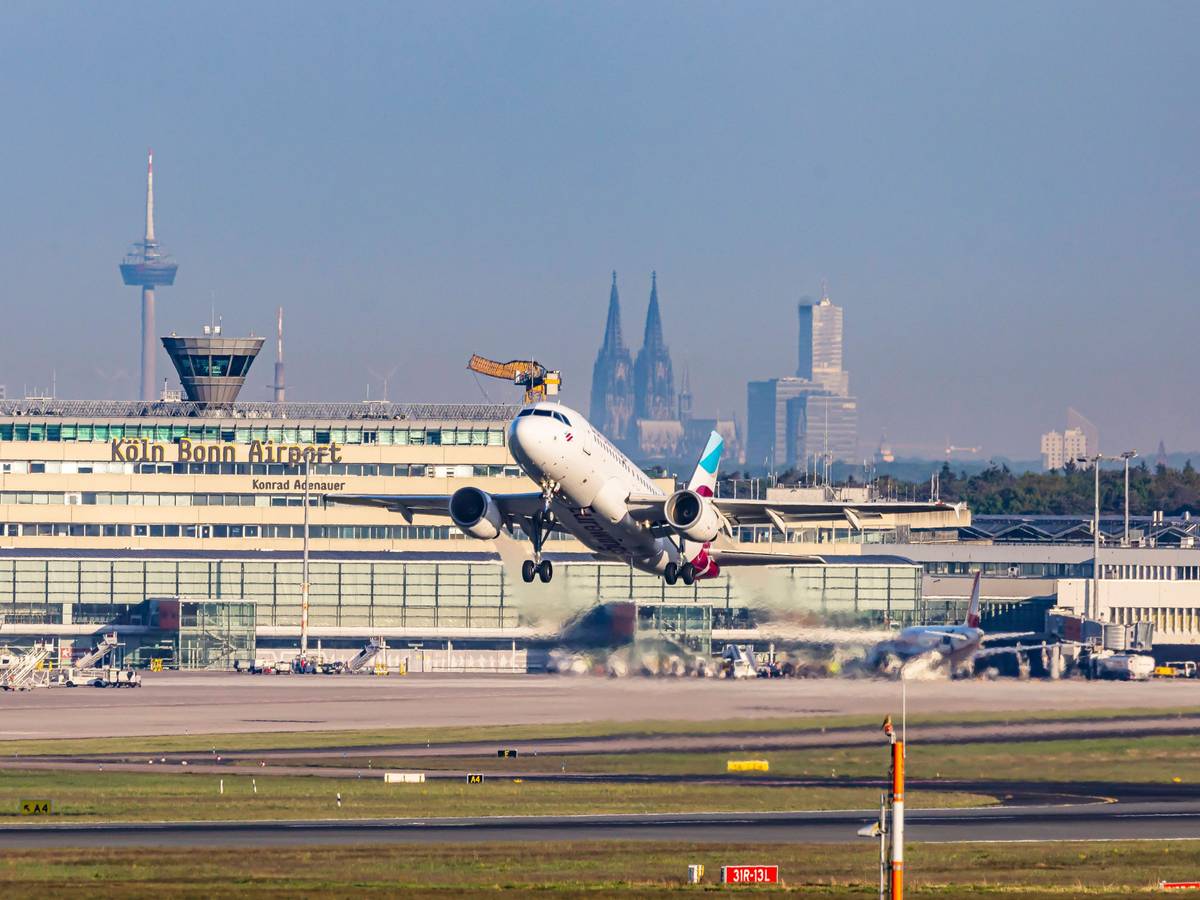 Ein Flugzeug hebt vom Flughafen Köln/Bonn ab. Im Hintergrund der Kölner Dom.