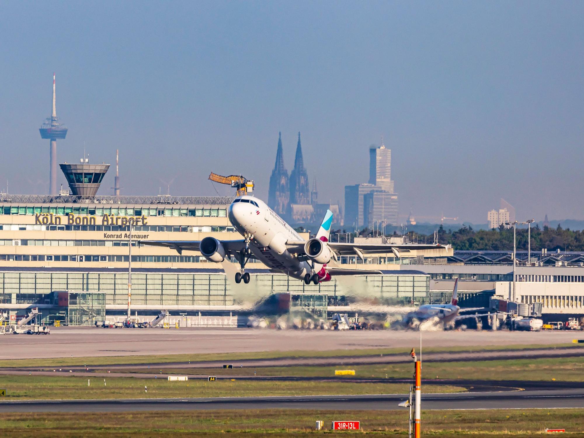 Ein Flugzeug hebt vom Flughafen Köln/Bonn ab. Im Hintergrund der Kölner Dom.