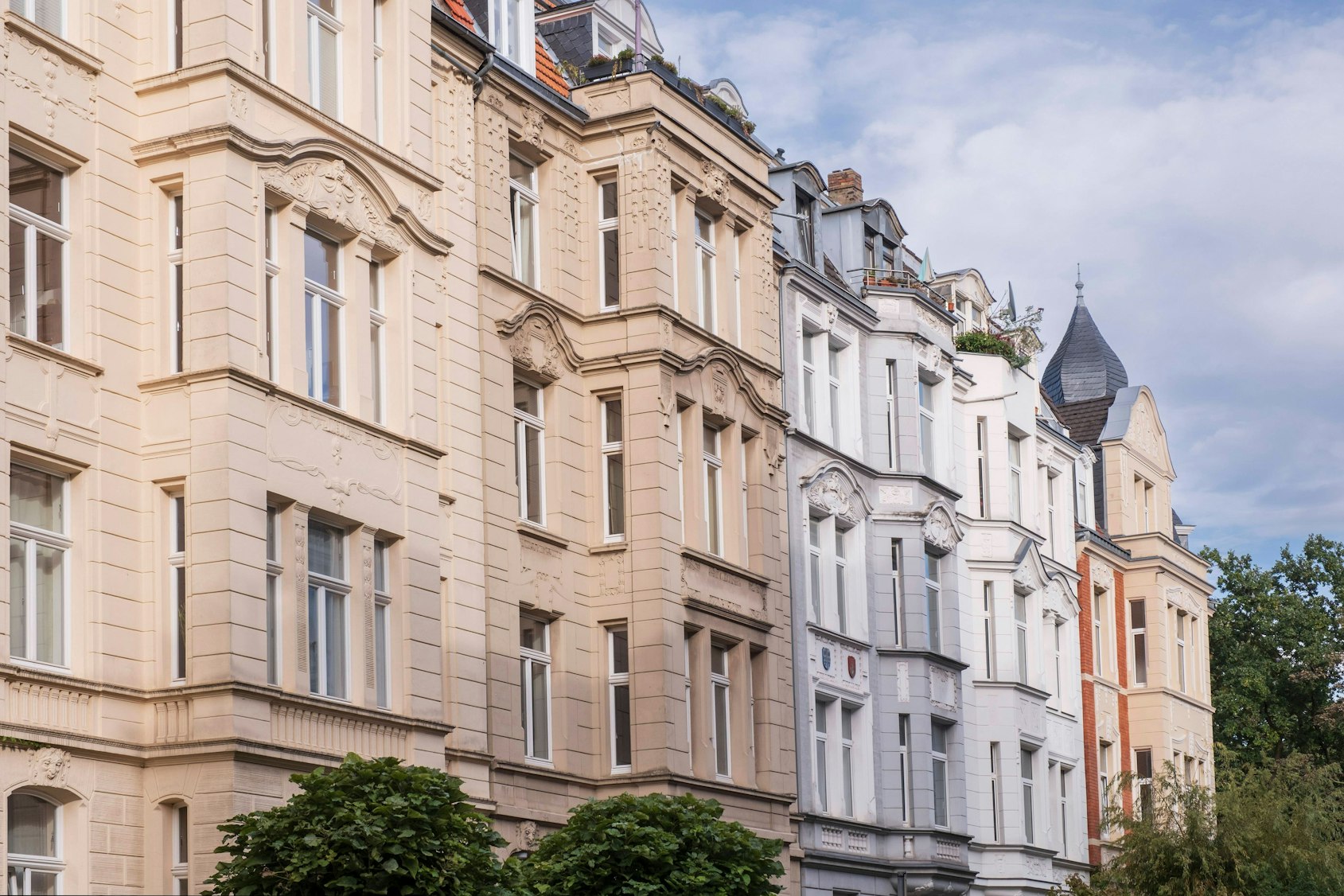 Reihe stilvoller Altbau-Mietshäuser mit detailreichen Fassaden unter leicht bewölktem Himmel