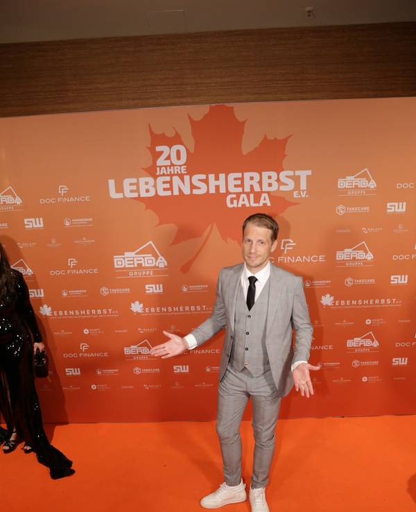 Ein Mann im Anzug steht vor einer Wand mit der Aufschrift Lebensherbst.
