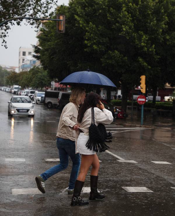 An einem regnerischen Tag auf Mallorca gehen Menschen mit Regenschirmen über eine Straße, auf der sich Wasser gesammelt hat.
