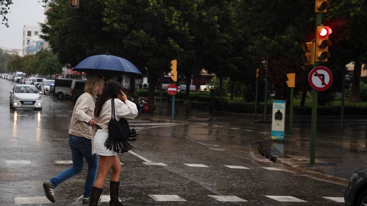 An einem regnerischen Tag auf Mallorca gehen Menschen mit Regenschirmen über eine Straße, auf der sich Wasser gesammelt hat.