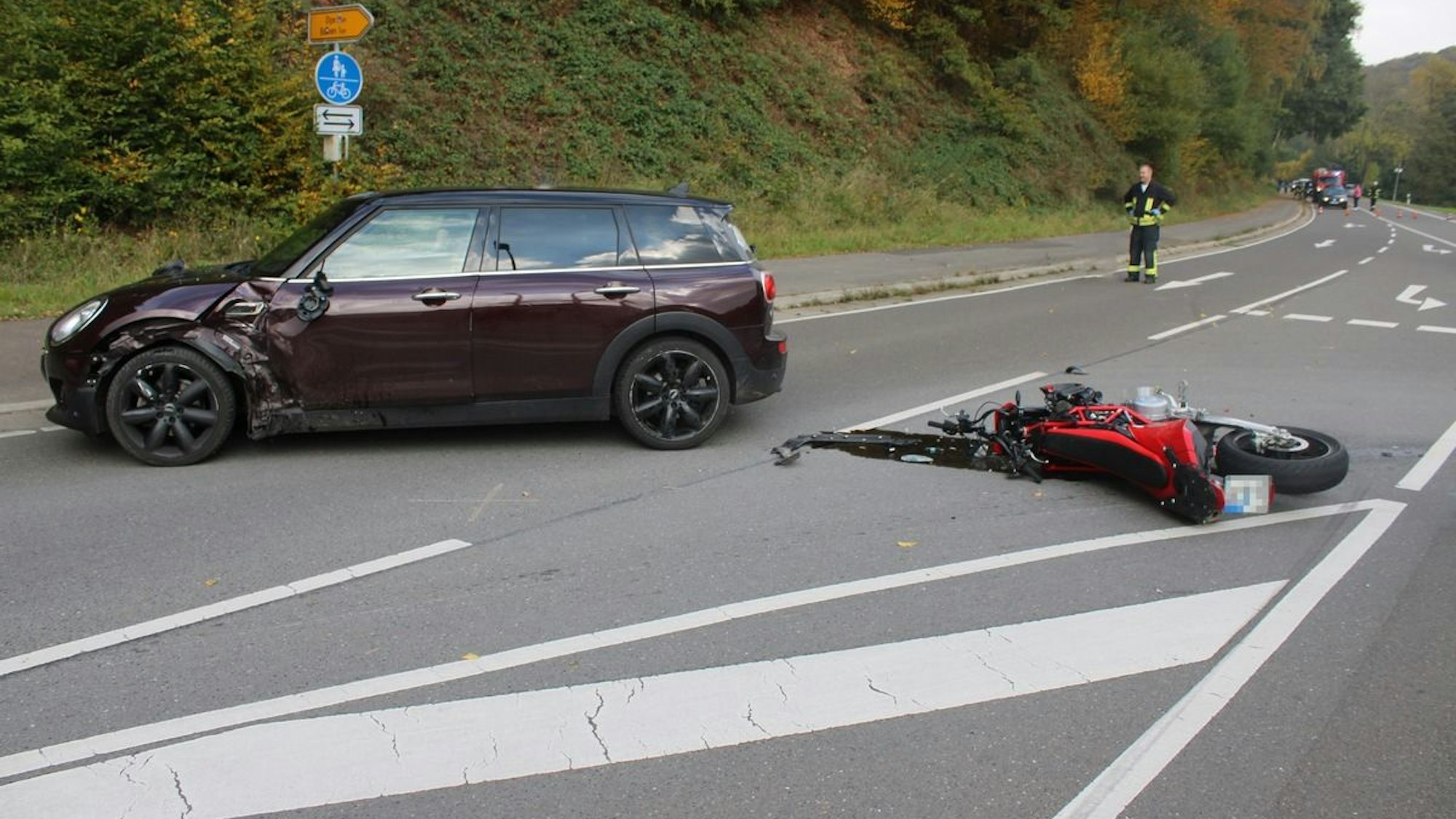 Ein Auto und ein Motorrad sind an einer Kreuzung zusammengestoßen. Trümmerteile liegen auf der Straße.
