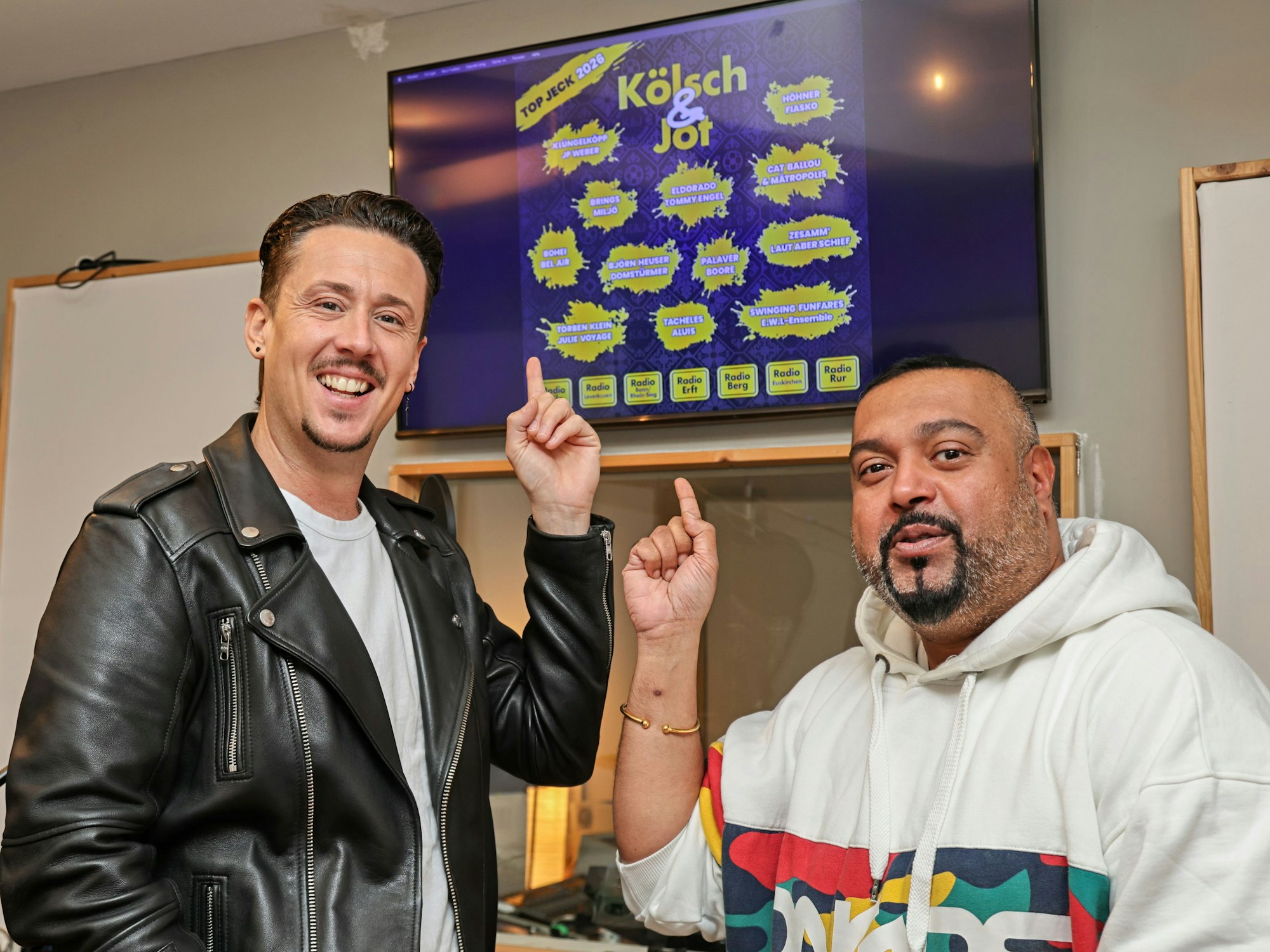 Manuel Sauer und Elvis Katticaren zeigen auf das Cover von „Kölsch & Jot – Top Jeck 2026“.