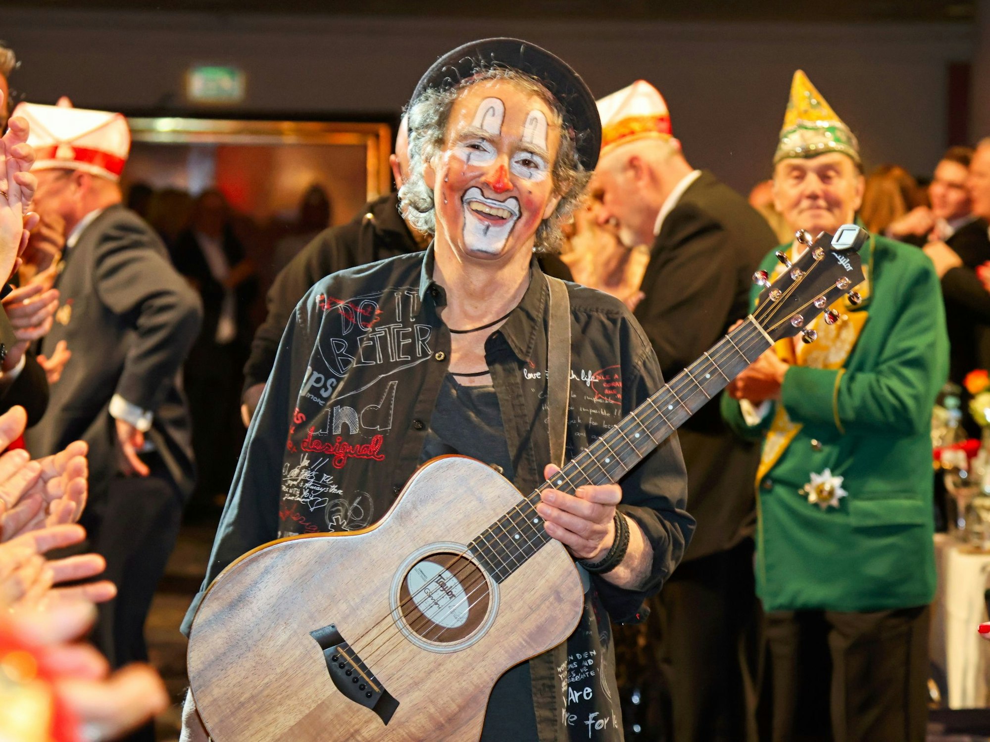 Peter Horn kommt mit Gitarre in einen Saal.