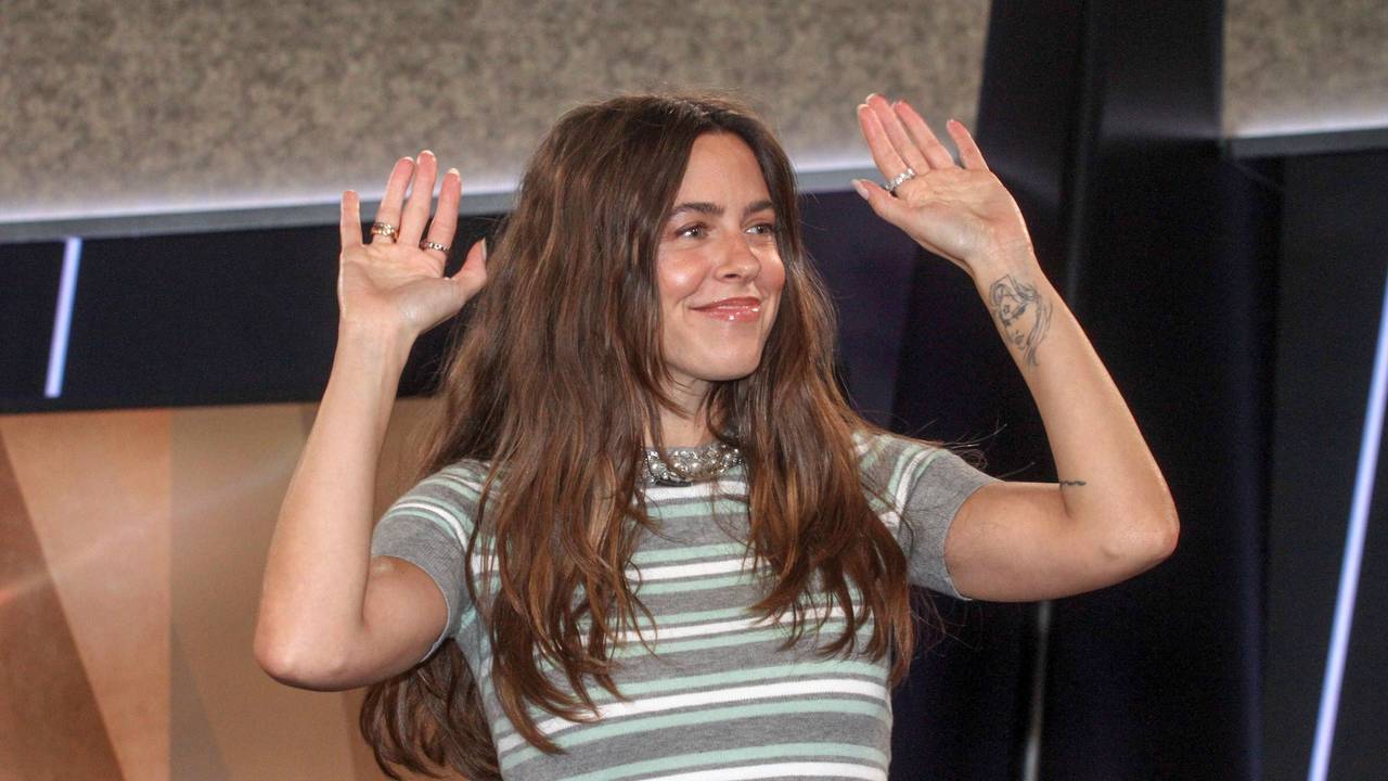 Vanessa Mai lächelt mit erhobenen Händen in einem gestreiften Crop-Top.