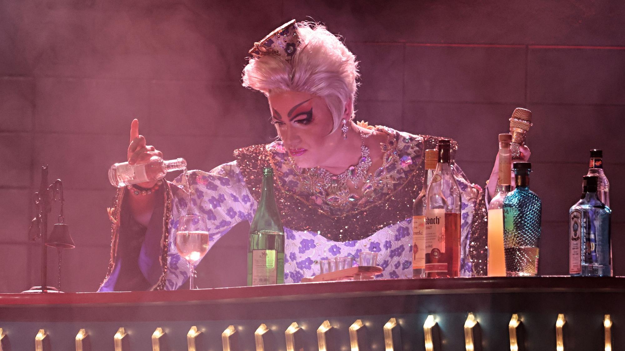 Julie Voyage gießt sich ein Getränk an der Bar ein.
