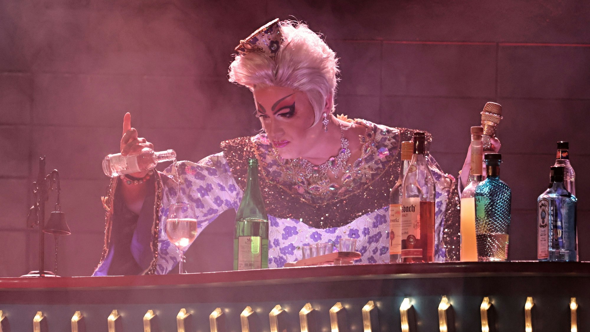 Julie Voyage gießt sich ein Getränk an der Bar ein.