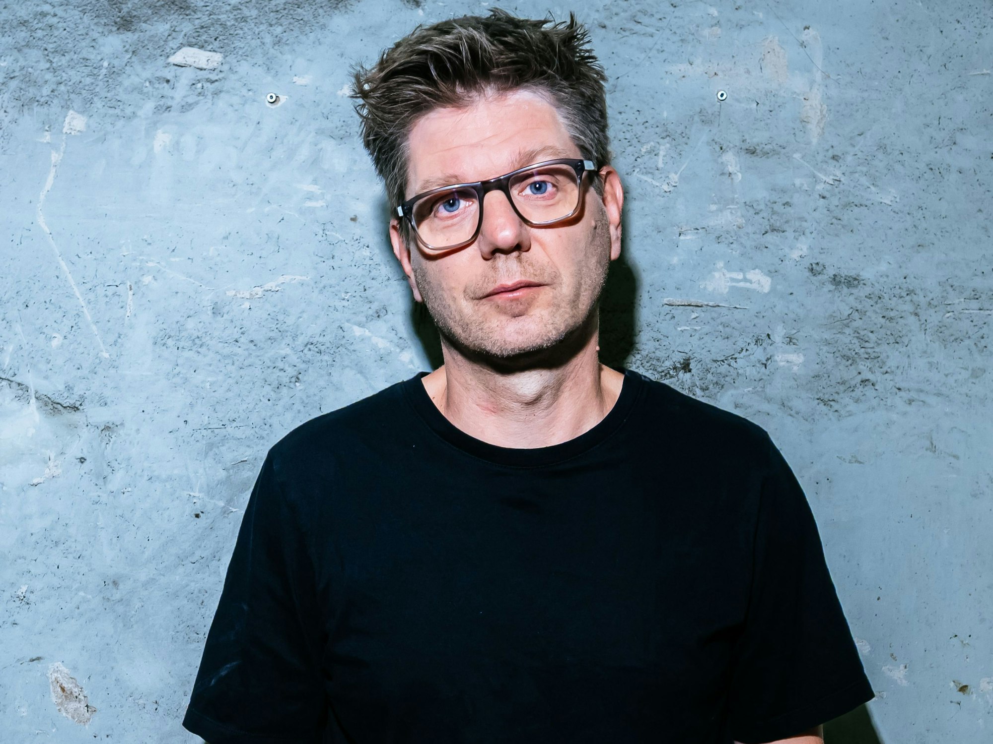 Pivo Deinert lehnt an einer Wand.